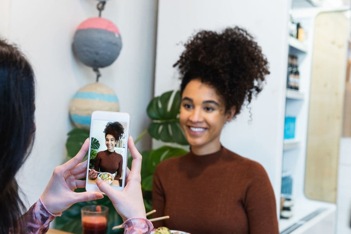 Eine junge Frau wird beim Essen in einem Sushi-Restaurant mit dem Smartphone fotografiert.