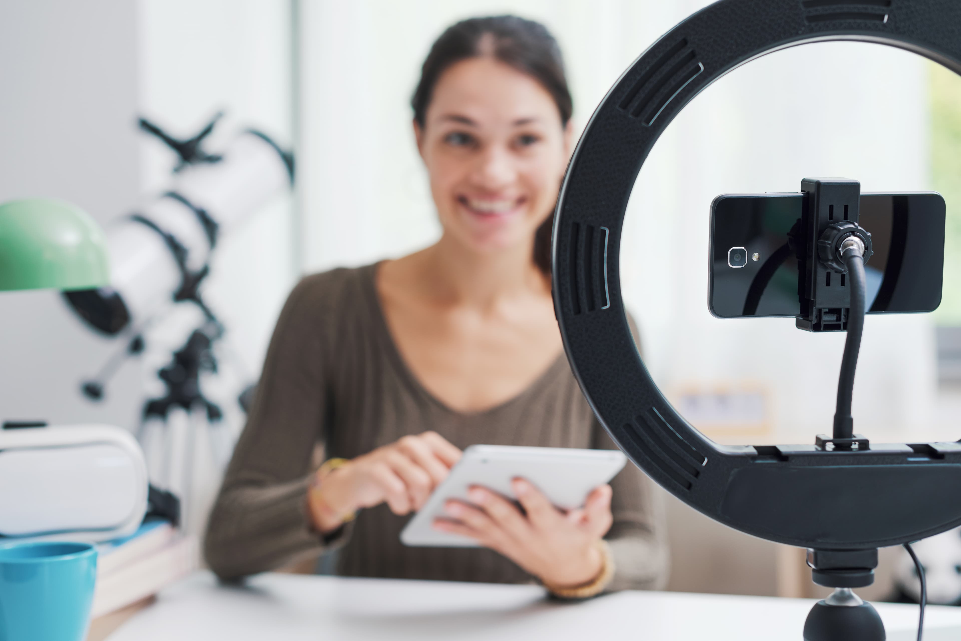 Junge Influencerin sitzt am Schreibtisch und erstellt Videos für ihre Follower in den sozialen Medien, sie lächelt und benutzt ein digitales Tablet