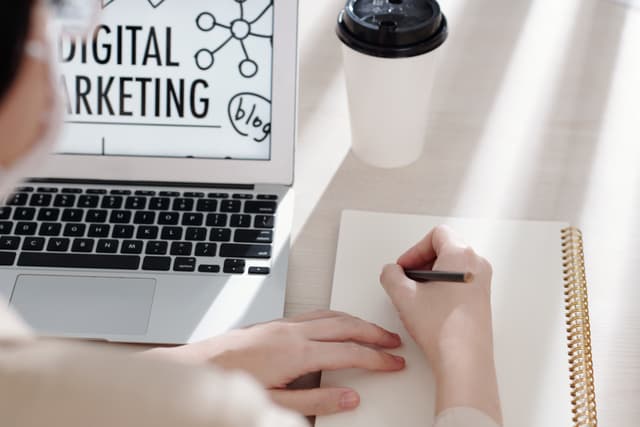 Online Marketing Manager erledigt Aufgaben am Schreibtisch: Laptop und Notizblick vor ihm