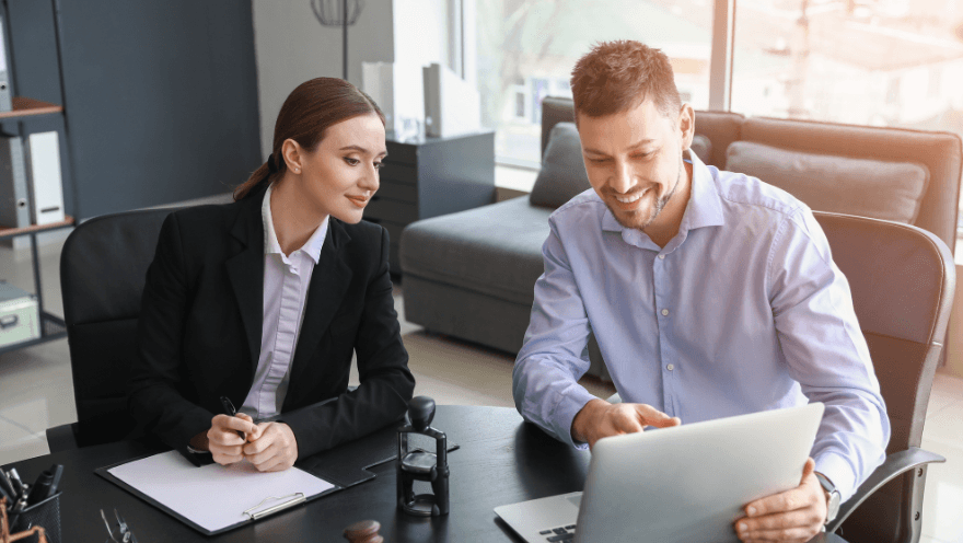 Mann und Frau in Business-Kleidung diskutieren vor einem Laptop in moderner Büroumgebung.